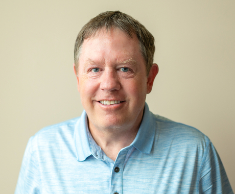 Photo of a man with brownish short hair, wearing a light colored polo shirt, smiling at the camera