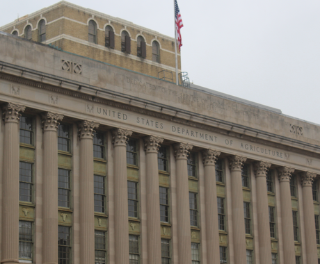 Edificio del USDA en Washington, D.C. Es un edificio grande de varias plantas con intrincadas columnas y ventanas en la fachada. En la parte superior, se puede leer el lema "UNITED STATES DEPARTMENT OF AGRICULTURE" (Departamento de Agricultura de los Estados Unidos). La bandera estadounidense ondea en un asta en el tejado.