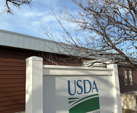 Un letrero blanco con las palabras "USDA SERVICE CENTER" y el logotipo verde de las colinas onduladas. Al fondo, un edificio de una sola planta con revestimiento marrón rojizo.