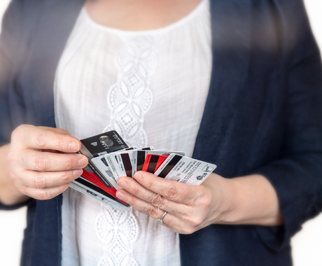 The bust of a woman, with a white blouse and black jacket, holding multiple credit cards fanned out betwen her hands