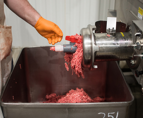 meat going through grinder into a bucket, man watching on