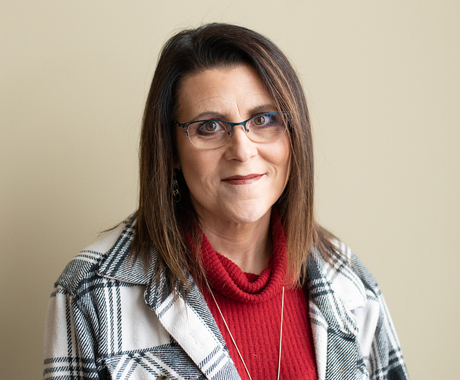 Woman wearing glasses in a white and black plaid blazer with a red shirt underneath poses for a picture