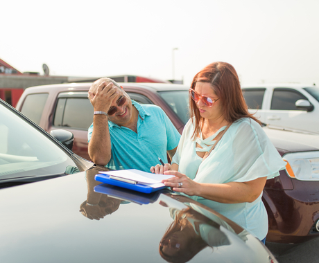 Man and woman filling out paperwork on hood of vehicle in a parking lot