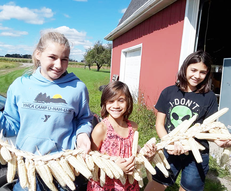 Three girls holding a string of corn with stalks braided