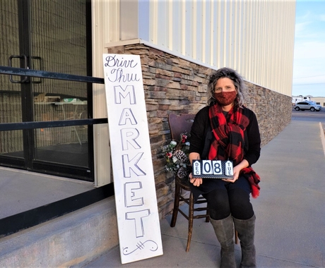 Woman with mask sitting outside next to Drive Thru Market sign