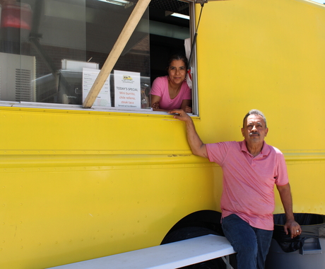 man and woman posing in front of and inside of a yellow food truck