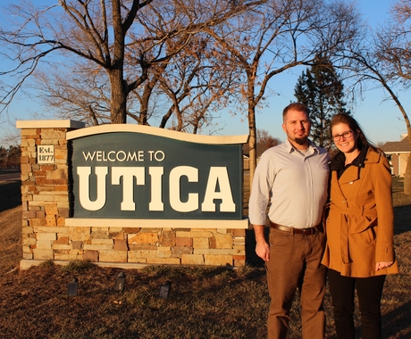 Man and Woman in front of town sign for "Utica"