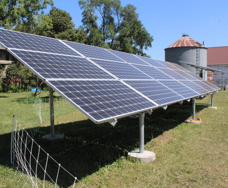 Solar panel with wire fencing around it, house and grain bin in background