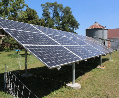 Solar panel with wire fencing around it, house and grain bin in background