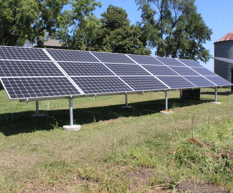 Solar panel with wire fencing around it, house and grain bin in background