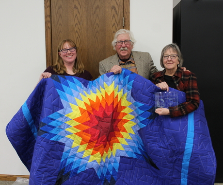 Two women and a men holding up a Native American Star Quilt.