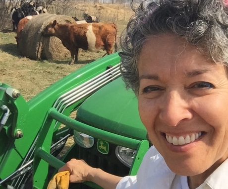 Woman on tractor smiles while cattle feed on hay in background
