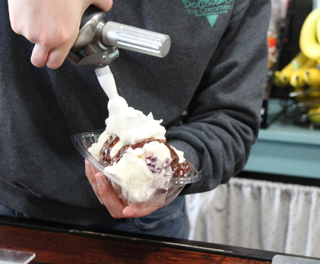 Employee sprays whip cream on top of ice cream sundae