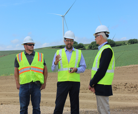 Three men in yellow vests and hard hats with wind turbine behind