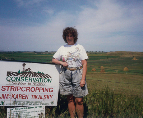 Woman standing beside Conservation sign in field
