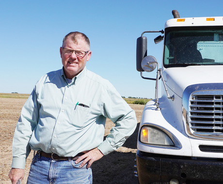 Man standing with hand on his hip in front of grain truck in harvested field
