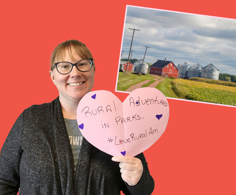 Woman holding a heart that says "Rural adventures in parks #LoveRuralAm"