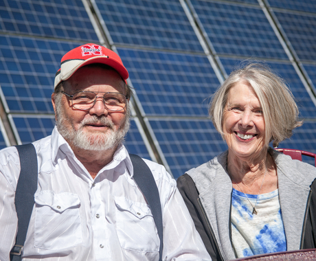 man and woman posing for picture in front of solar panel