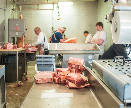 Red meat sitting on a counter with people processing meat in the background