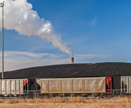 A hill of black coal, delivered by silver and red train cars in the foreground, waiting to be fed into a power plant