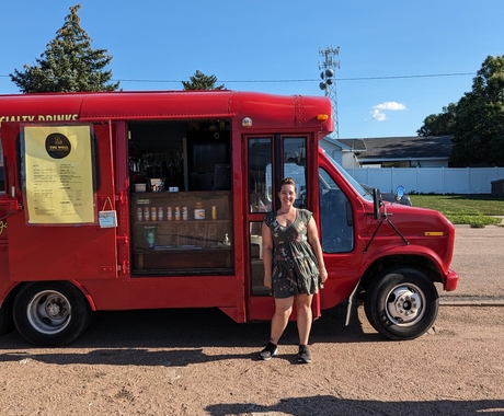 Woman standing in front of a red renovated bus that is a coffee shop