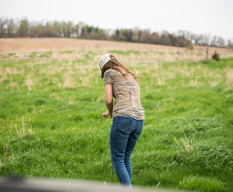 Woman wearing hat, T-shirt and jeans examining grazing grasses