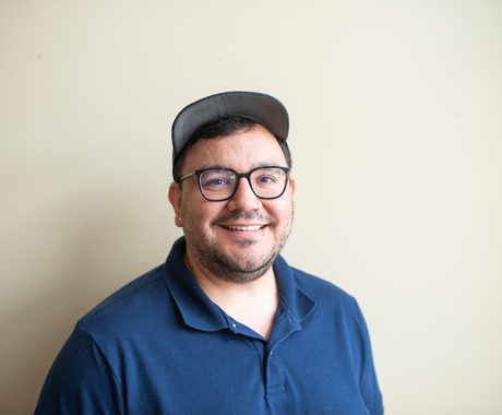 Man in dark polo with cap and dark rimmed glasses poses smiling for a picture