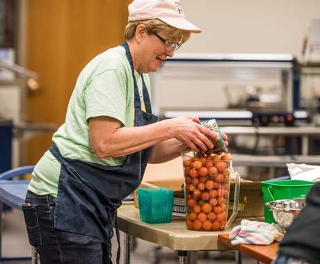 Woman cafeteria worker adding cherry tomatoes to a clear container for lunch service