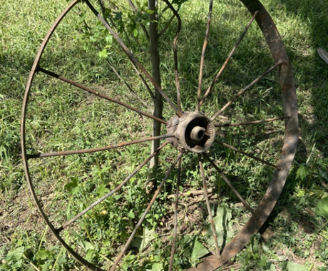 A metal wagon wheel that's a little bent, leaning against a fence post