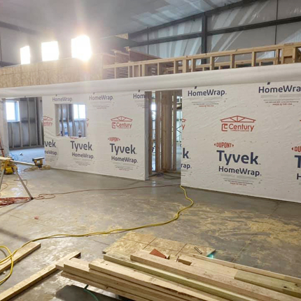 Inside of a shop under construction with wallboard up, 2x4s on the ground, a ladder, and a saw