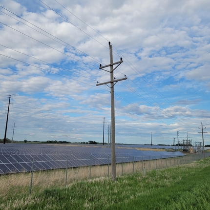 Solar panels and transmission lines in a field under a cloudy blue sky