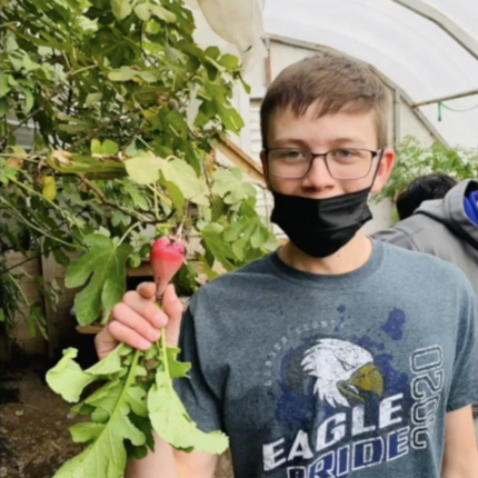 Middle school boy wearing a black facial mask holding a radish