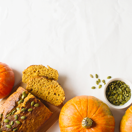 Pumpkins and loaf of bread with pumpkin seeds on top on white background