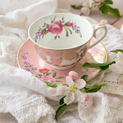 Taza de té de flores rosas y blancas y plato encima de un paño cerca de flores sobre una mesa de madera. Foto: chaiko - stock.adobe.com