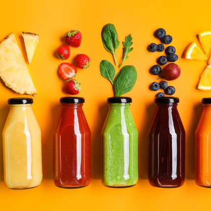 Five juice bottles with different juice colors and fruit above with orange background
