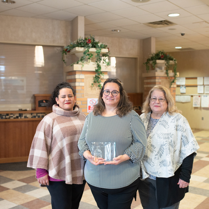 Tres mujeres posan para una foto en el vestíbulo de una oficina con un galardón en mano. 