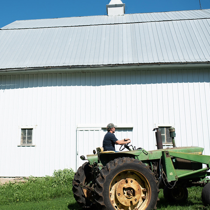 Farmer on a tractor with a building in the background.