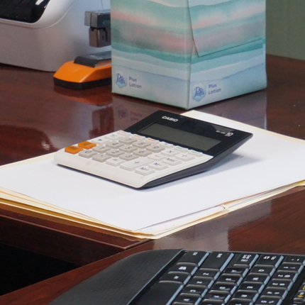 Articulos arriba en un escritorio incluyendo una parte de un teclado, una calculadora encima de unas carpetas blancas, una caja de pañuelos desechables