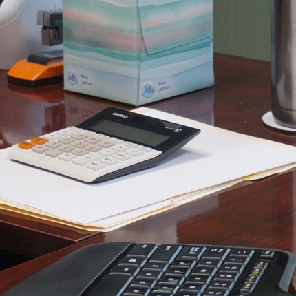 Imagen de una calculadora arriba de un escritorio con papeles y varias cosas alrededor