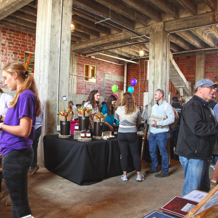 An inside room with exposed wooden rafters and brick walls holds tables covered in items with people shopping at the tables