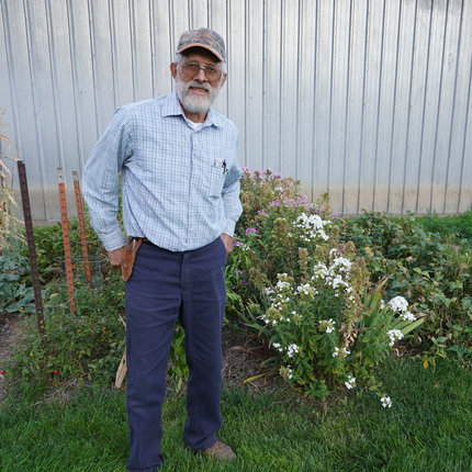 Dennis Demmel posa para una foto con una camisa de manga larga azul claro y jeans oscuros en un jardín.