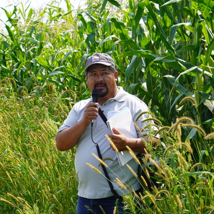 Man speaking into microphone with corn in the background