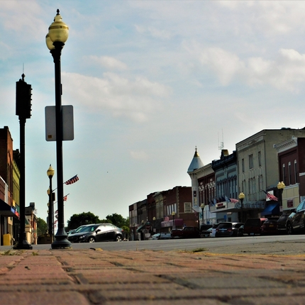 View of a rural Main Street from the street level with lamp posts on the right and buildings on both sides of the street.