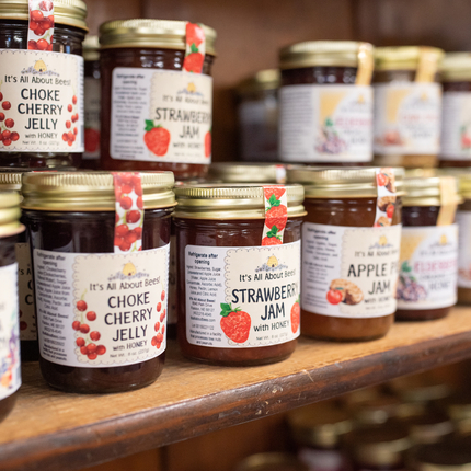 Small jars of a variety of fruit jams stacked on top of each other on a wooden shelf.