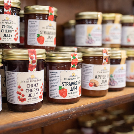 Jars of jelly lined up on a shelf, stacked 2 jars high and about 3 jars deep