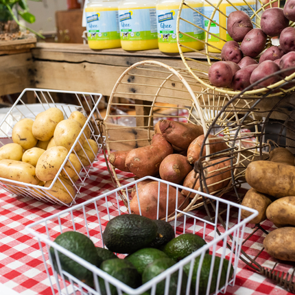 Una variedad de patatas yacían en diferentes cestas de alambre blanco, una de ellas con aguacates en el frente sobre un mantel rojo y blanco.