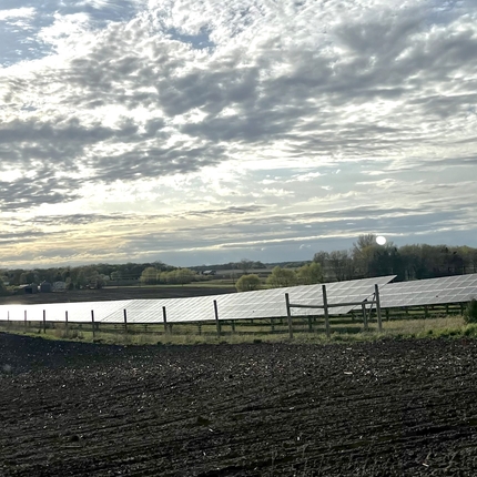 Paneles solares con tierras de cultivo en primer plano y un hermoso cielo nublado con tonos amarillos y azules en el cielo