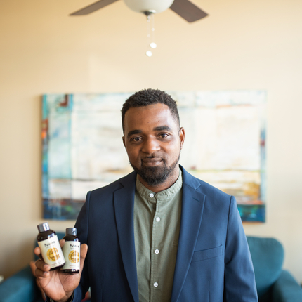Man in a suit jacket holding two small bottles of vanilla, in a living room