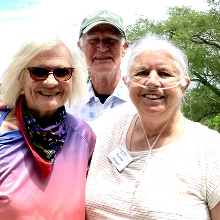 Three people smiling and looking at the camera, two women in front and a man in a hat behind