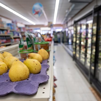 A photo looking down an aisle in a grocery store. Pears are in the left foreground. On the right are coolers full of packaged food.